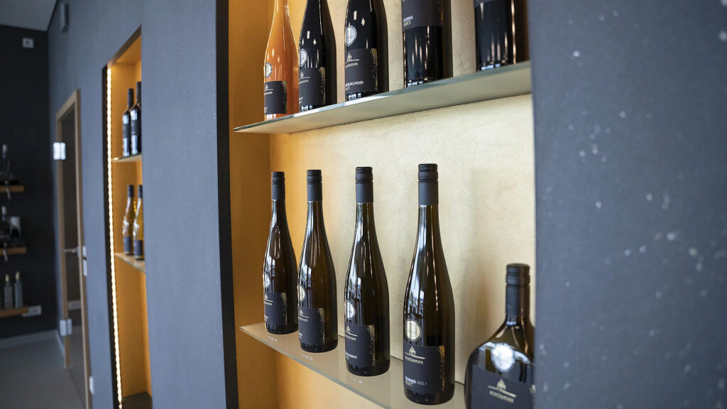 Goldene Regale in der Vinothek vom Weingut Schürmer - Einrichtung aus Eiche in modern mit großzügiger Theke und Nero Assoluto Natursteinarbeitsplatte von Strasser